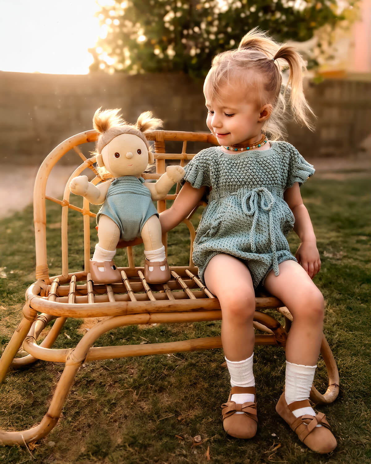 toddler sitting with doll wearing hand knited baby clothes by JuneBee Baby artisan clothing